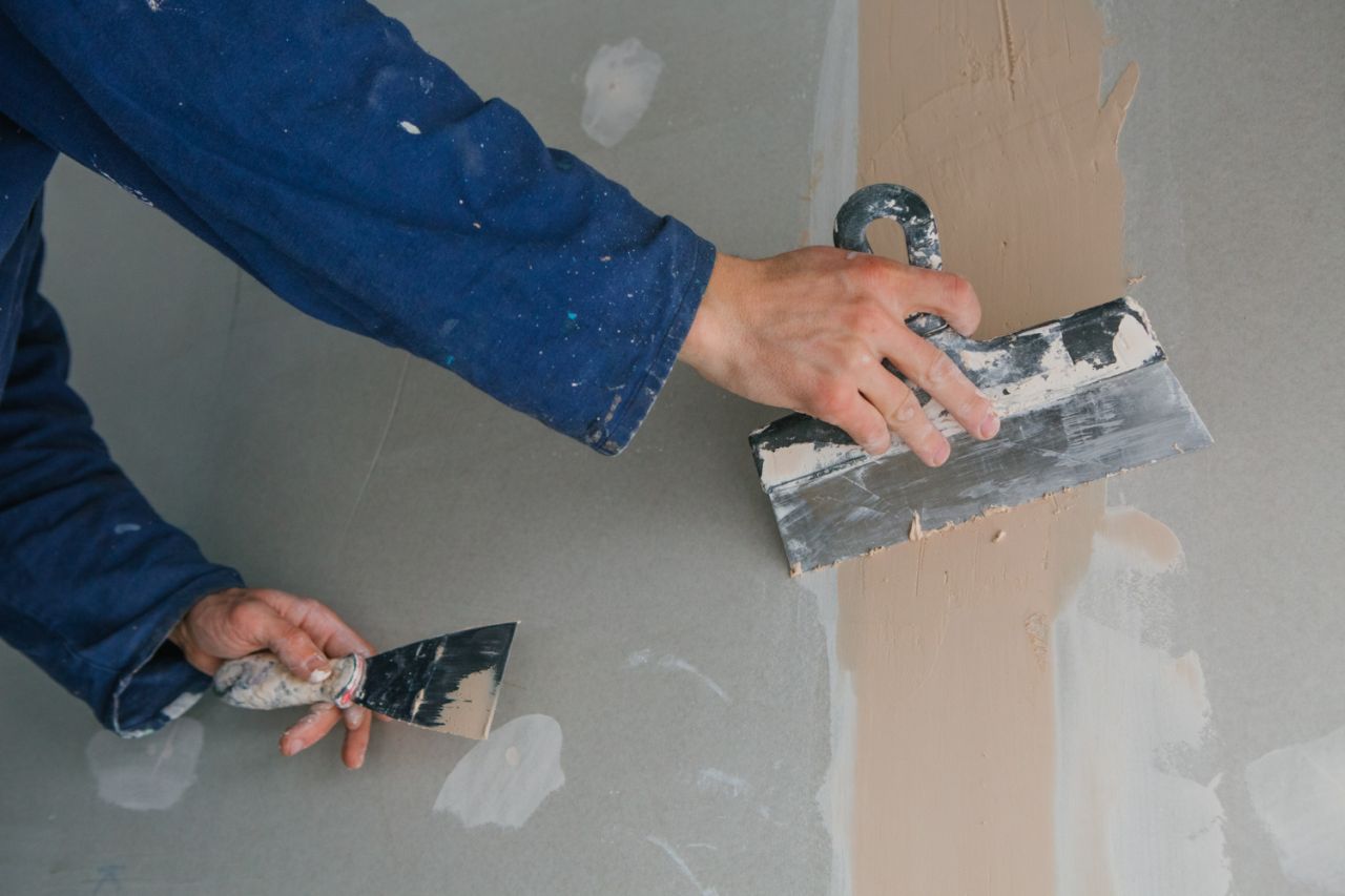 plasterer man works plastering two trowels plasterboard blue uniform (1)